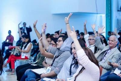 Personas participan de un evento y alzan las manos ante una pregunta