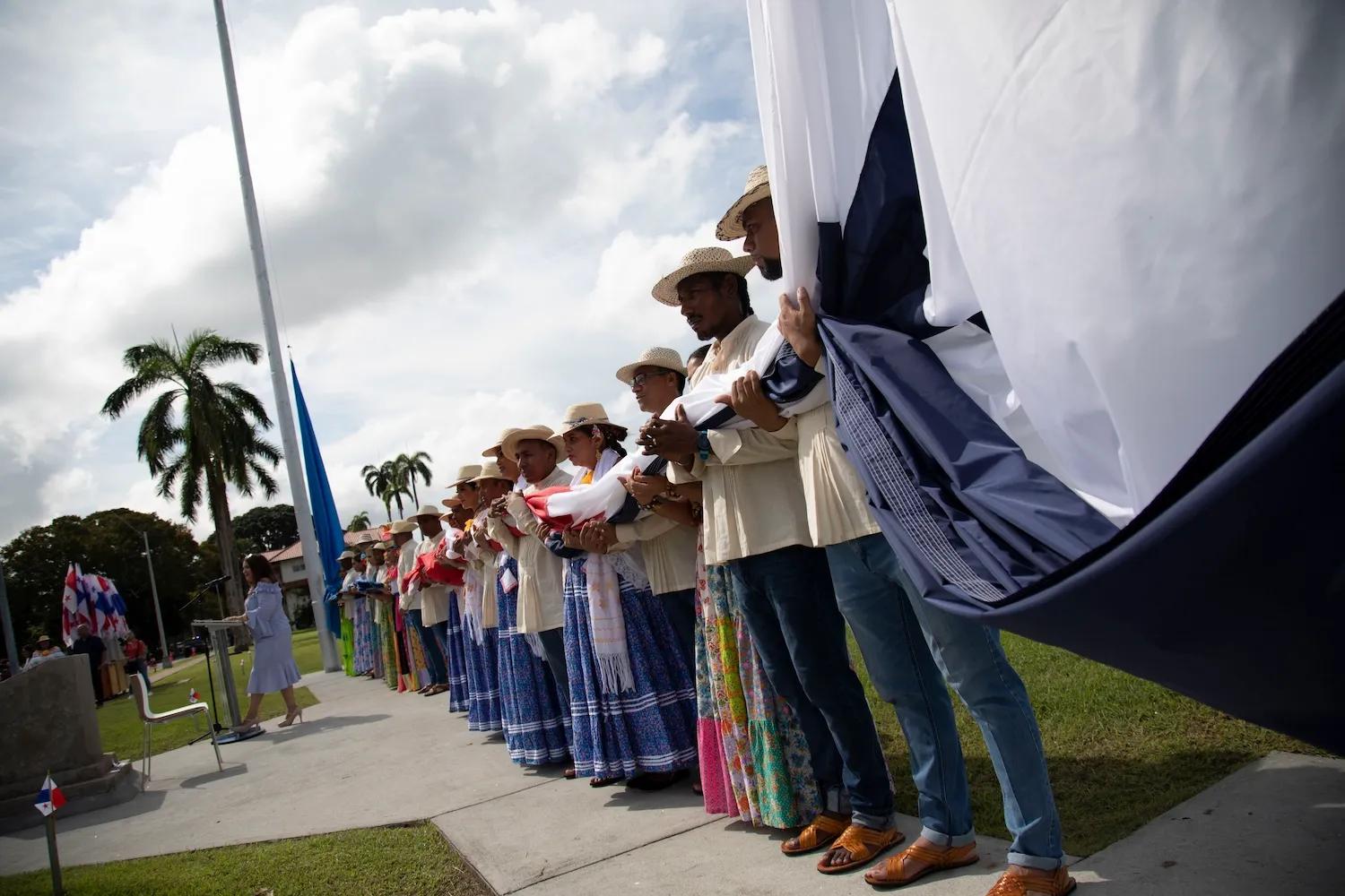 Personas carga con sus manos la bandera mientras se preparan para izarla