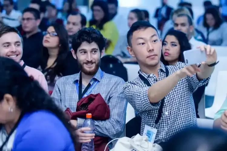 Dos hombre en una conferencia sostienen un teléfono celular para tomar una foto